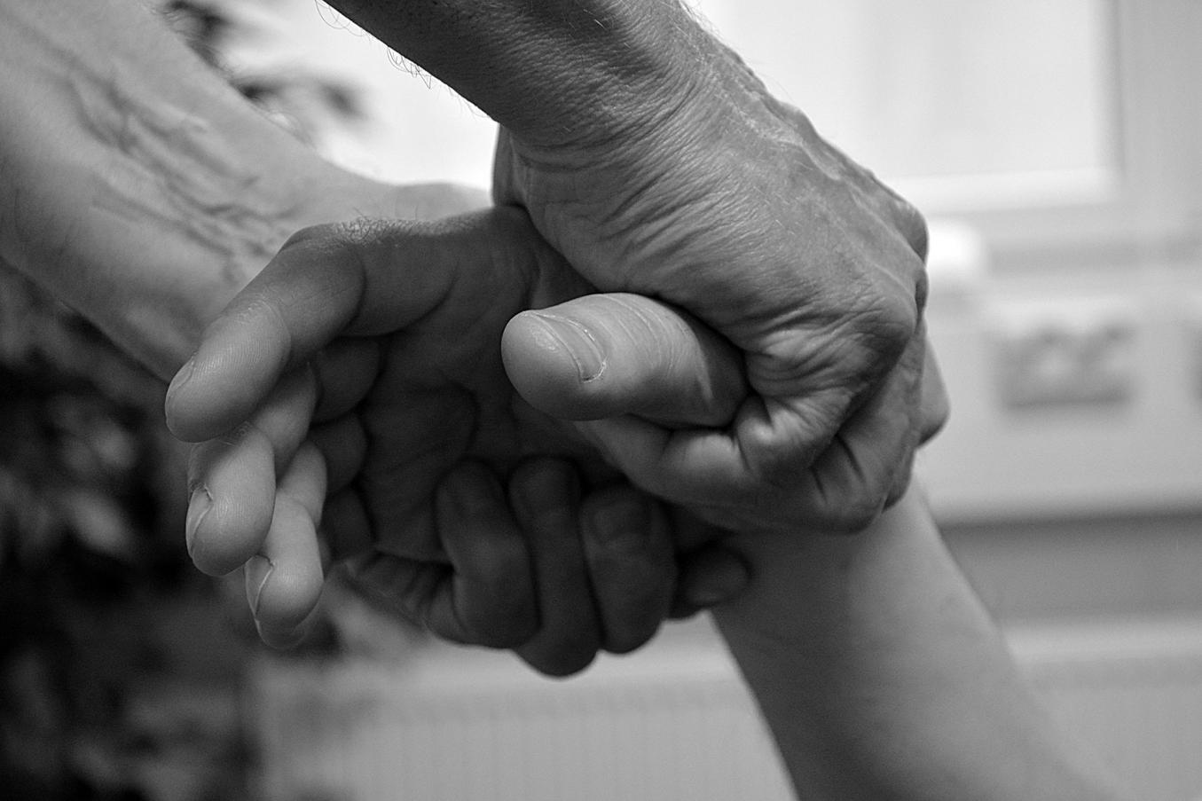 Koskettava palveluammatti - henkilö pitää kaksin käsin kiinni toisen henkilön oikeasta kädestä.